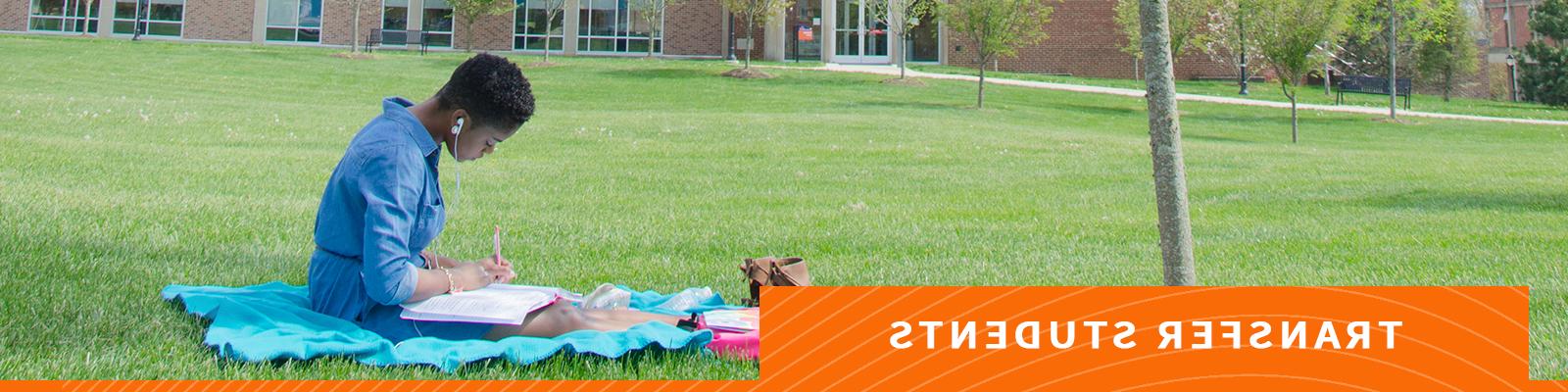 Student studying on blanket in grass area on campus